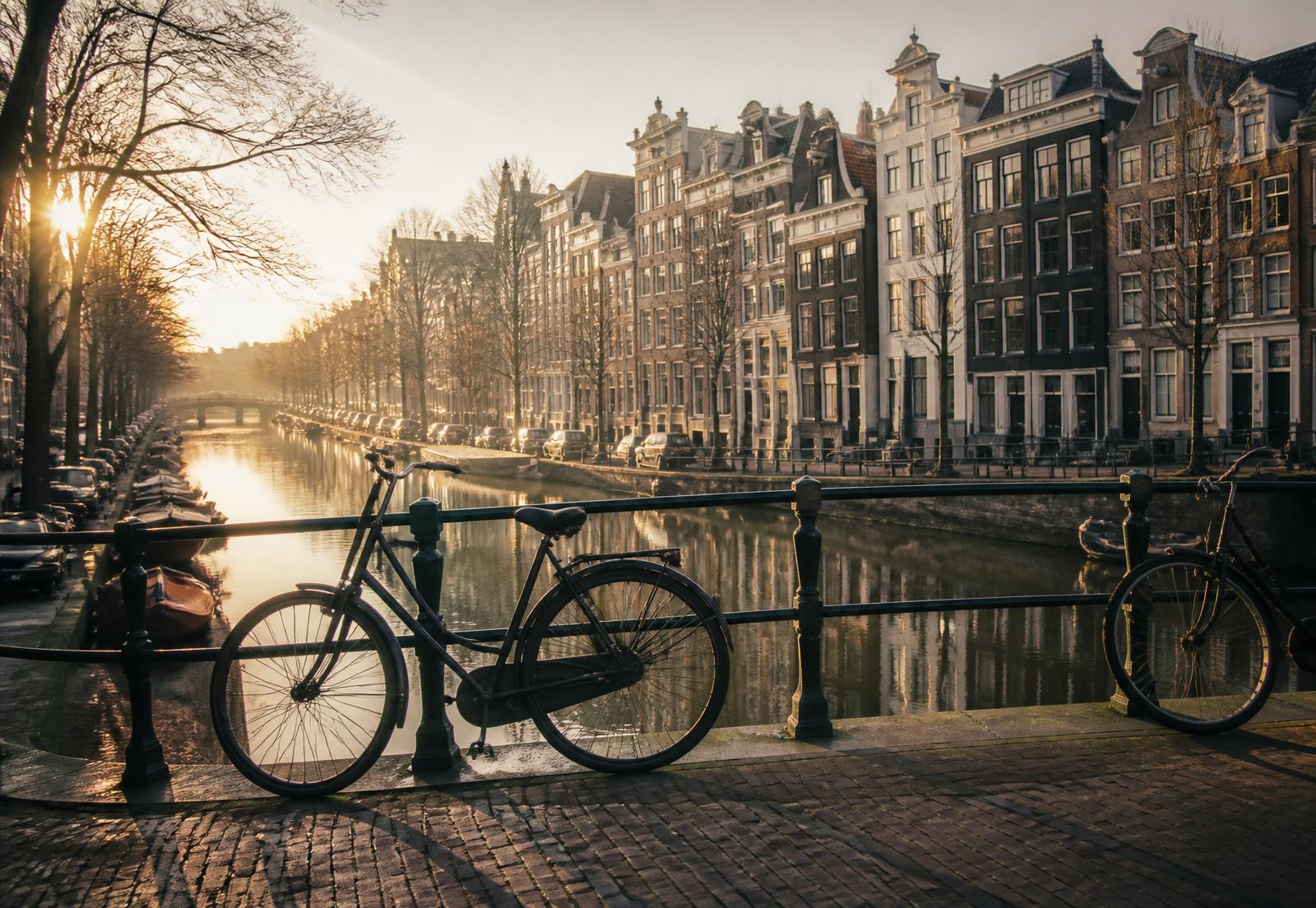 Bicycles resting on a bridge over an Amsterdam canal at sunrise
